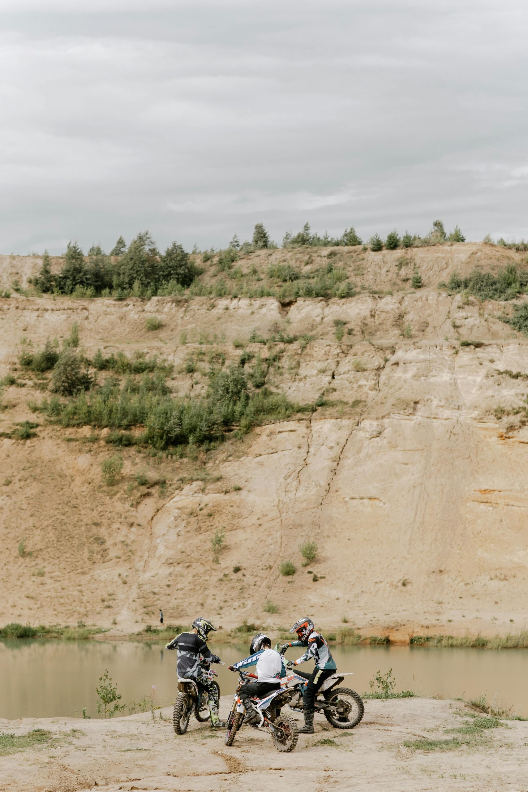 Three motocross riders pause near a scenic lakeside cliff, capturing the spirit of adventure and off-road exploration.